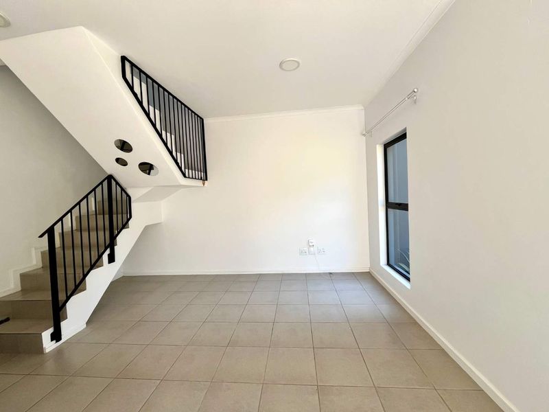 An open-plan living area featuring neutral tiled flooring, a modern staircase with a metal balustrade, and natural light from a side window.