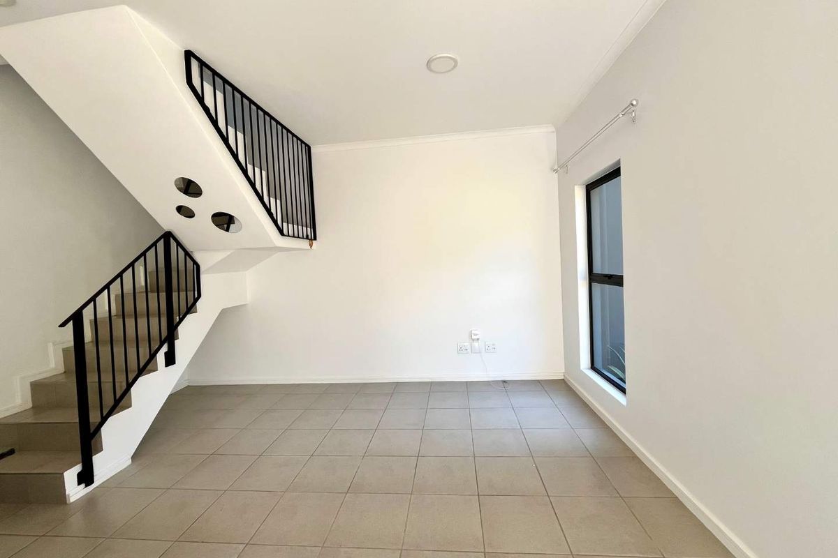 An open-plan living area featuring neutral tiled flooring, a modern staircase with a metal balustrade, and natural light from a side window.