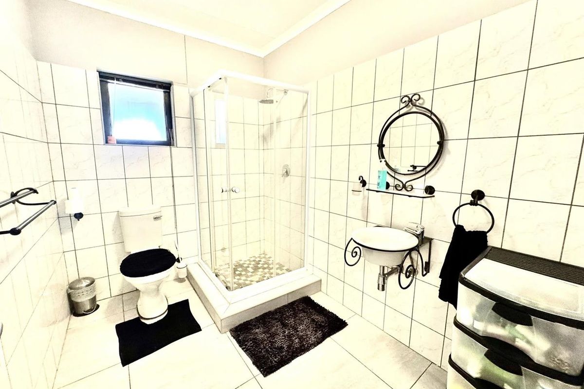 A functional bathroom featuring a glass-enclosed shower, wall-mounted basin, and toilet with full-height wall tiling.
