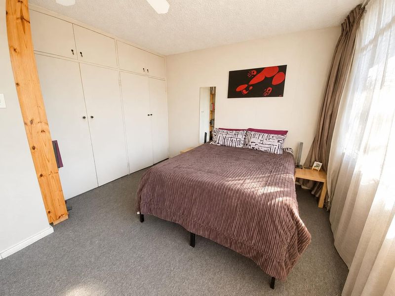 A functional bedroom featuring built-in cupboards, carpeted flooring, and a ceiling fan, offering a comfortable and practical living space.