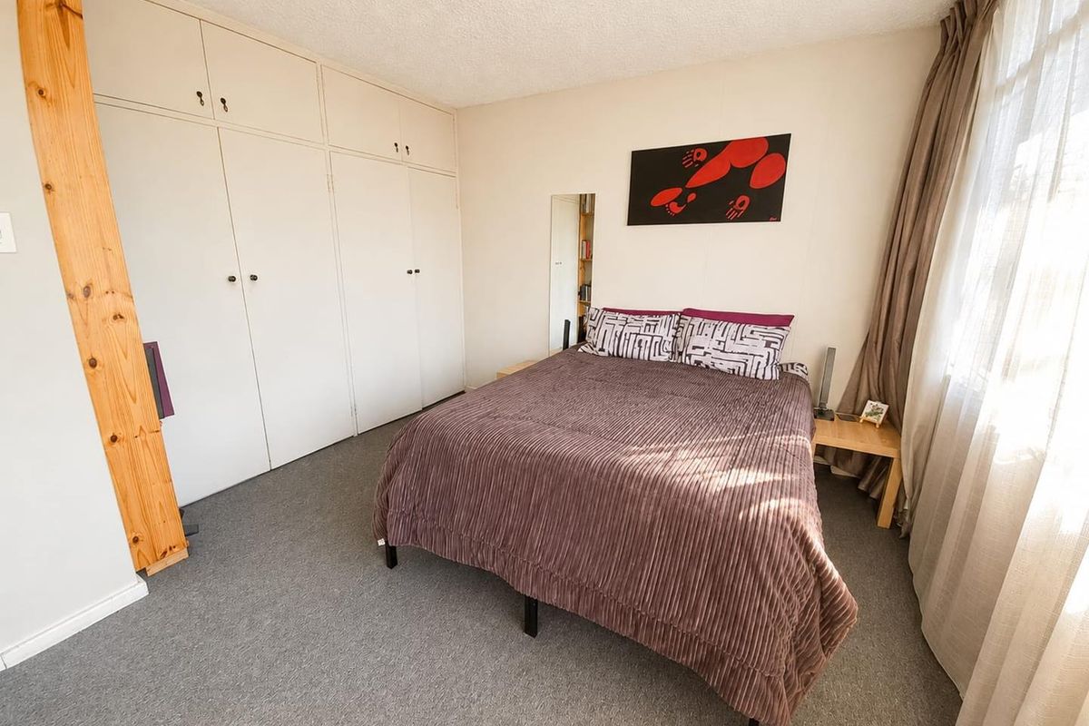 A functional bedroom featuring built-in cupboards, carpeted flooring, and a ceiling fan, offering a comfortable and practical living space.