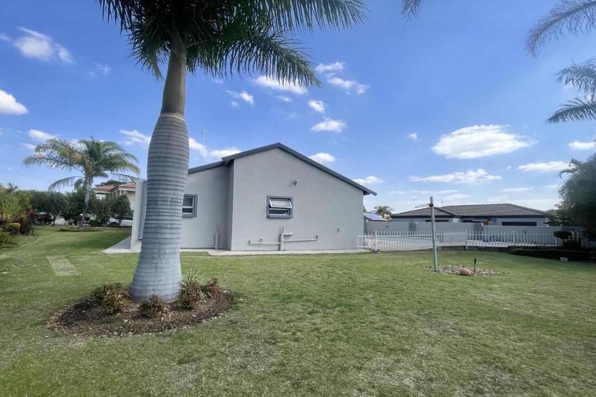 A view of the rear exterior of the townhouse, featuring a well-maintained lawn, established palm tree, and perimeter fencing.
