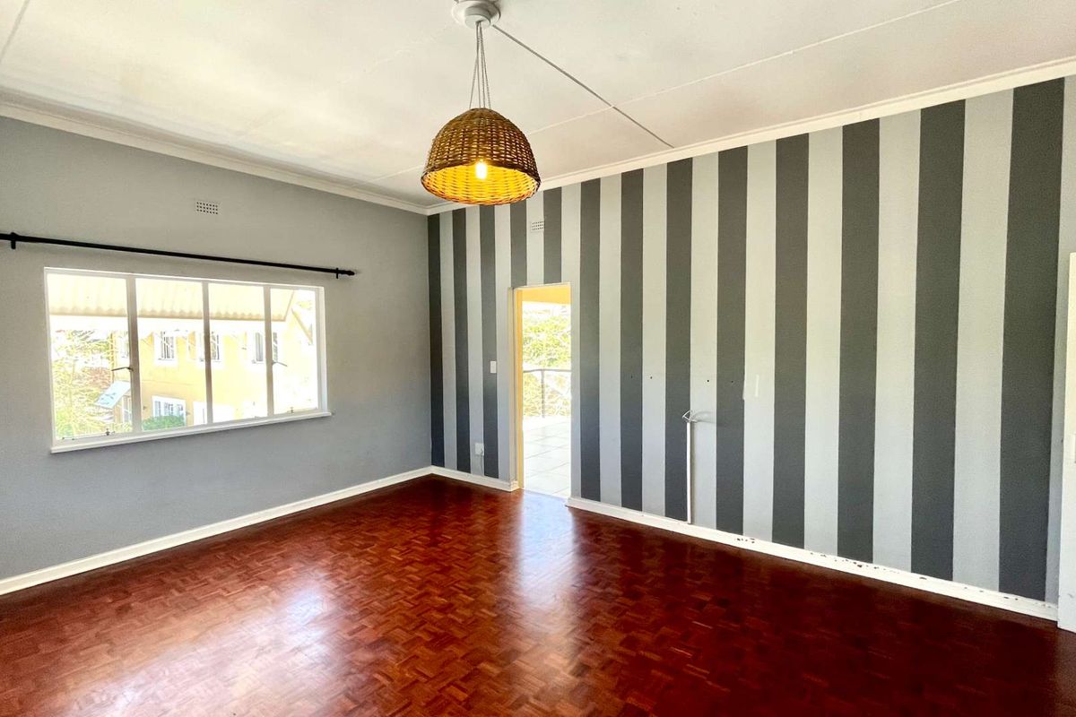 A spacious living room featuring polished parquet flooring, a striped feature wall, and large windows providing natural light.