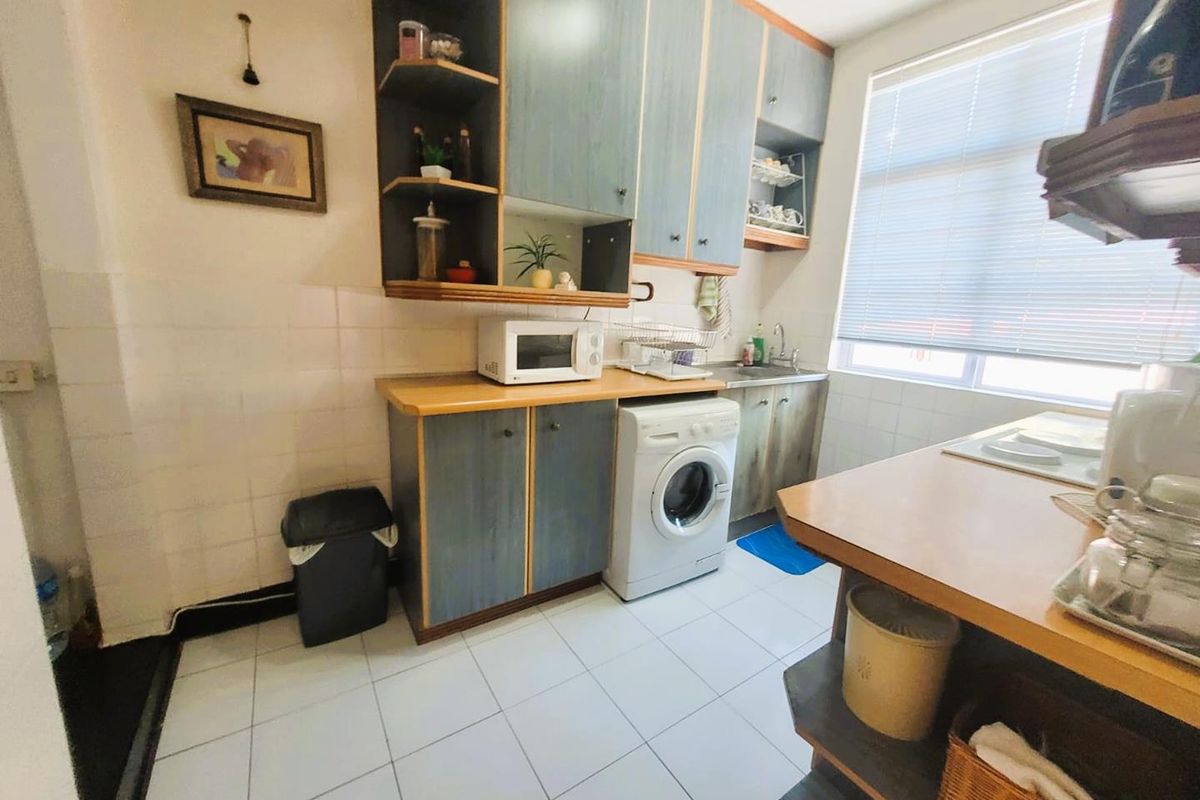 A functional kitchen featuring built-in cabinetry, tiled flooring, a stainless steel sink, and space for a washing machine.