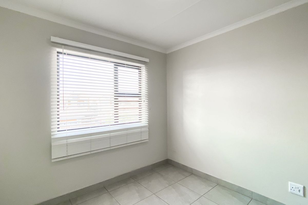A bright, empty bedroom featuring neutral wall tones, tiled flooring, and fitted venetian blinds, offering a clean and versatile space.
