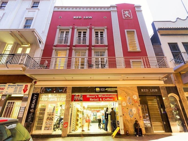 Street-level view of the Red Lion building featuring a prominent red facade, upper-level balconies, and ground-floor retail commercial spaces.