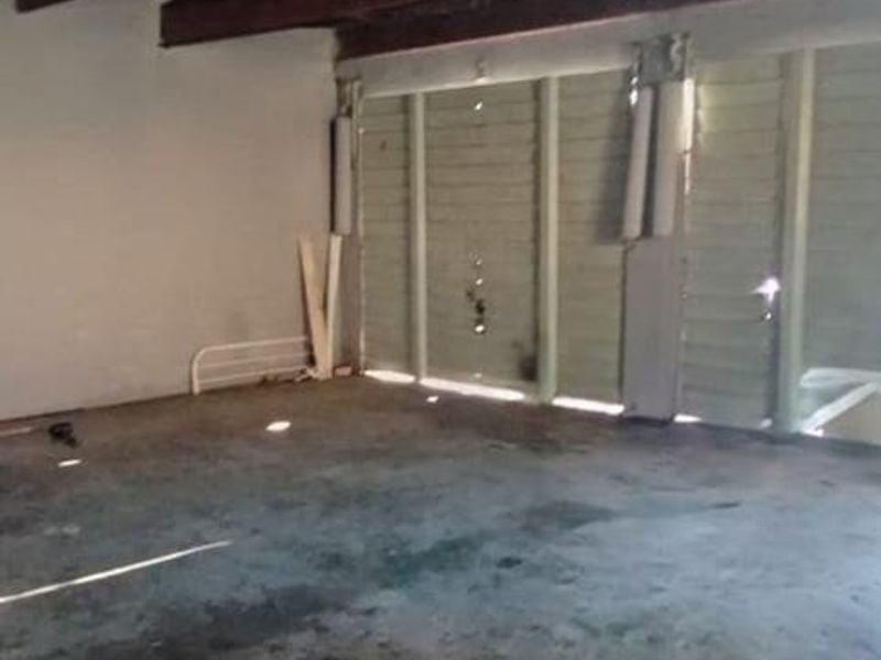 An empty, unfinished garage space featuring exposed timber ceiling beams, concrete flooring, and a damaged garage door.