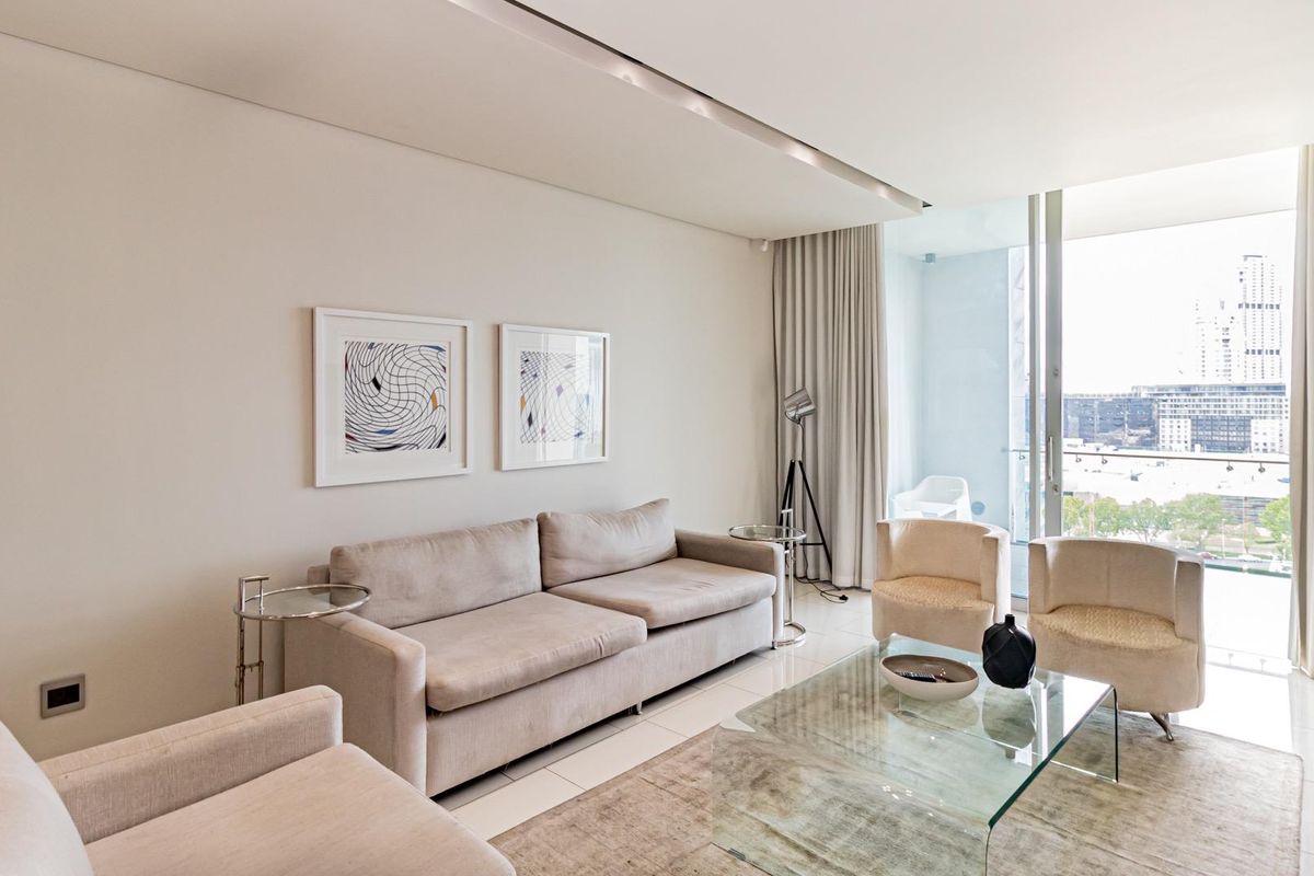 A bright and modern living room featuring large floor-to-ceiling glass sliding doors that open onto a balcony with city views.