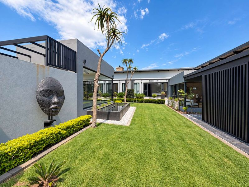 A beautifully landscaped rear garden featuring a modern water feature, manicured lawn, and covered patio areas with contemporary architectural design.