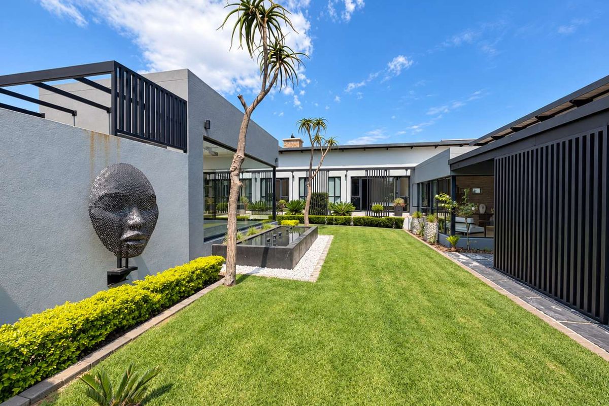 A beautifully landscaped rear garden featuring a modern water feature, manicured lawn, and covered patio areas with contemporary architectural design.