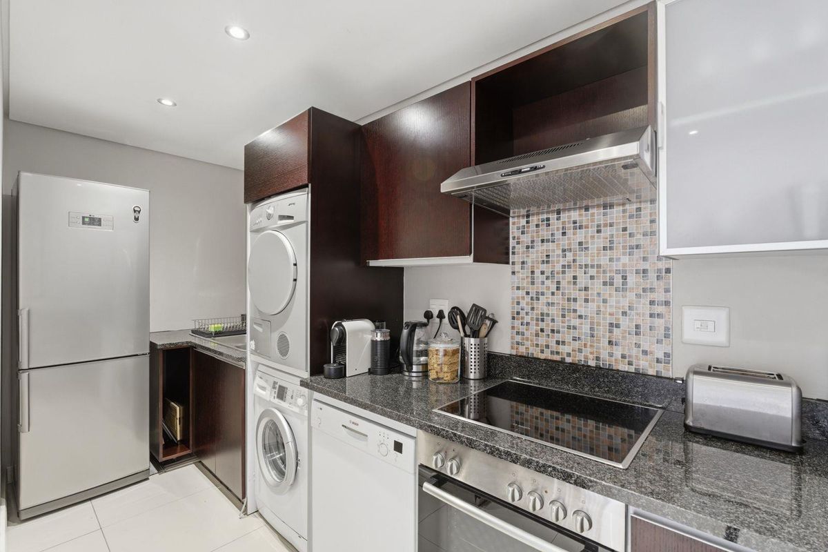 Modern kitchen featuring dark wood cabinetry, granite countertops, mosaic tile backsplash, and integrated appliances including an oven, hob, and laundry units.
