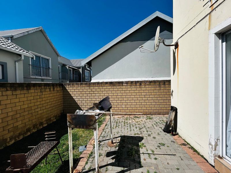A rear courtyard area featuring a paved patio, brick boundary wall, and exterior wall with visible rust staining and maintenance requirements.