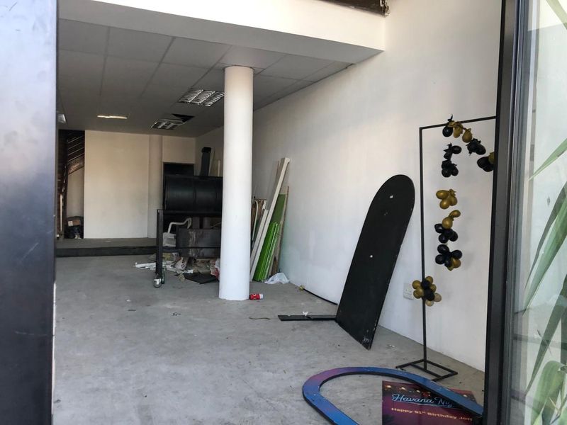 An empty retail space featuring a structural column, suspended ceiling with recessed lighting, and concrete flooring, currently requiring maintenance and cosmetic updates.