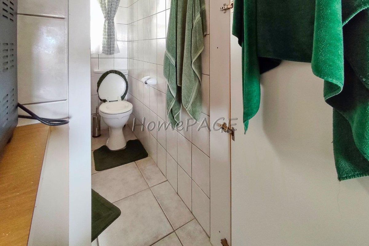A functional bathroom featuring tiled walls and flooring, equipped with a standard toilet and window for natural ventilation.