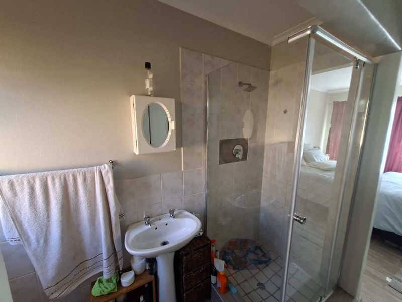 A functional bathroom featuring a pedestal basin and a glass-enclosed shower with tiled walls.