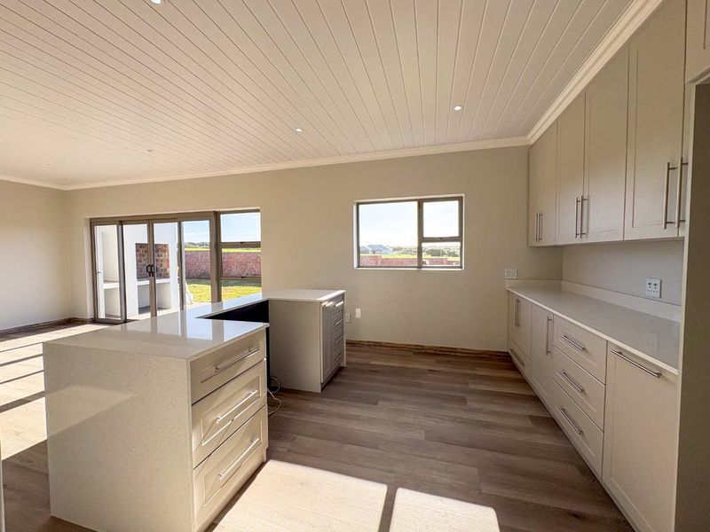 Modern open-plan kitchen featuring light-toned cabinetry, stone countertops, and wood-look flooring, with direct access to an outdoor patio area.