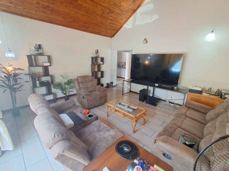 Spacious living room featuring a high vaulted timber ceiling and neutral tiled flooring, offering a comfortable and airy atmosphere.