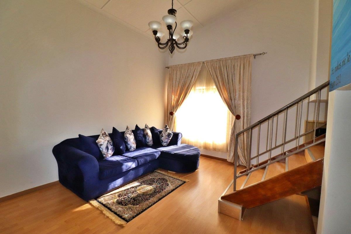 A living room featuring laminate flooring, a staircase with a metal railing, and a classic chandelier.