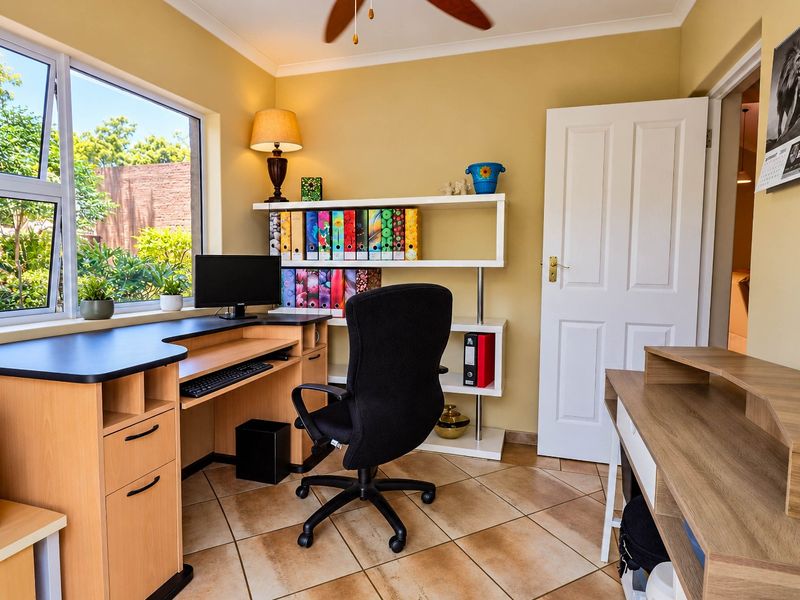 A functional home office featuring tiled flooring, a large window providing natural light, and built-in shelving for storage.