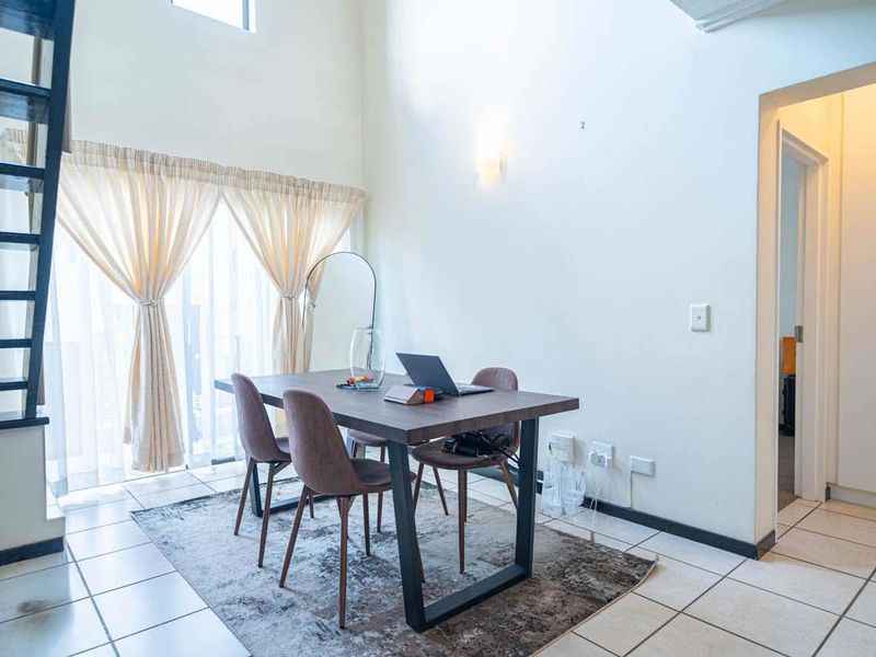 Open-plan living area featuring double volume ceilings, tiled flooring, a staircase, and built-in storage cupboards.