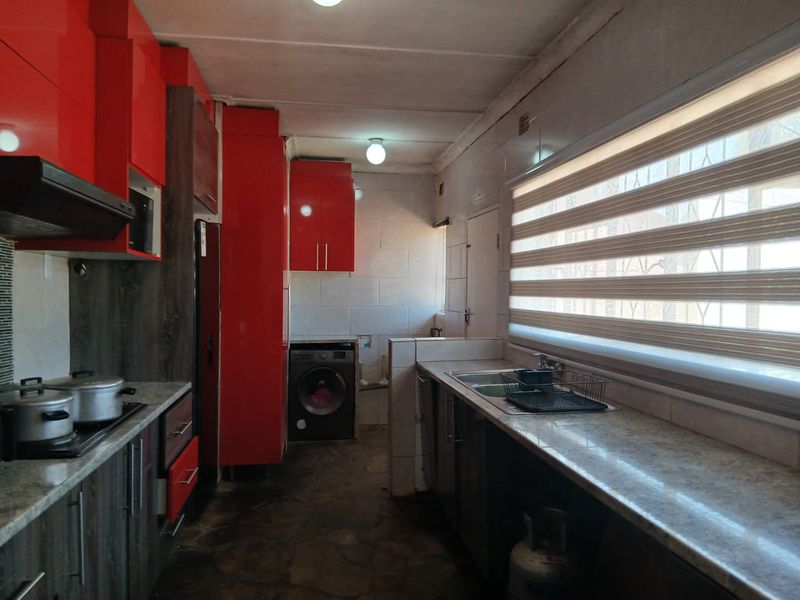A functional kitchen featuring vibrant red cabinetry, stone countertops, a double sink, and integrated cooking appliances with tiled finishes throughout.