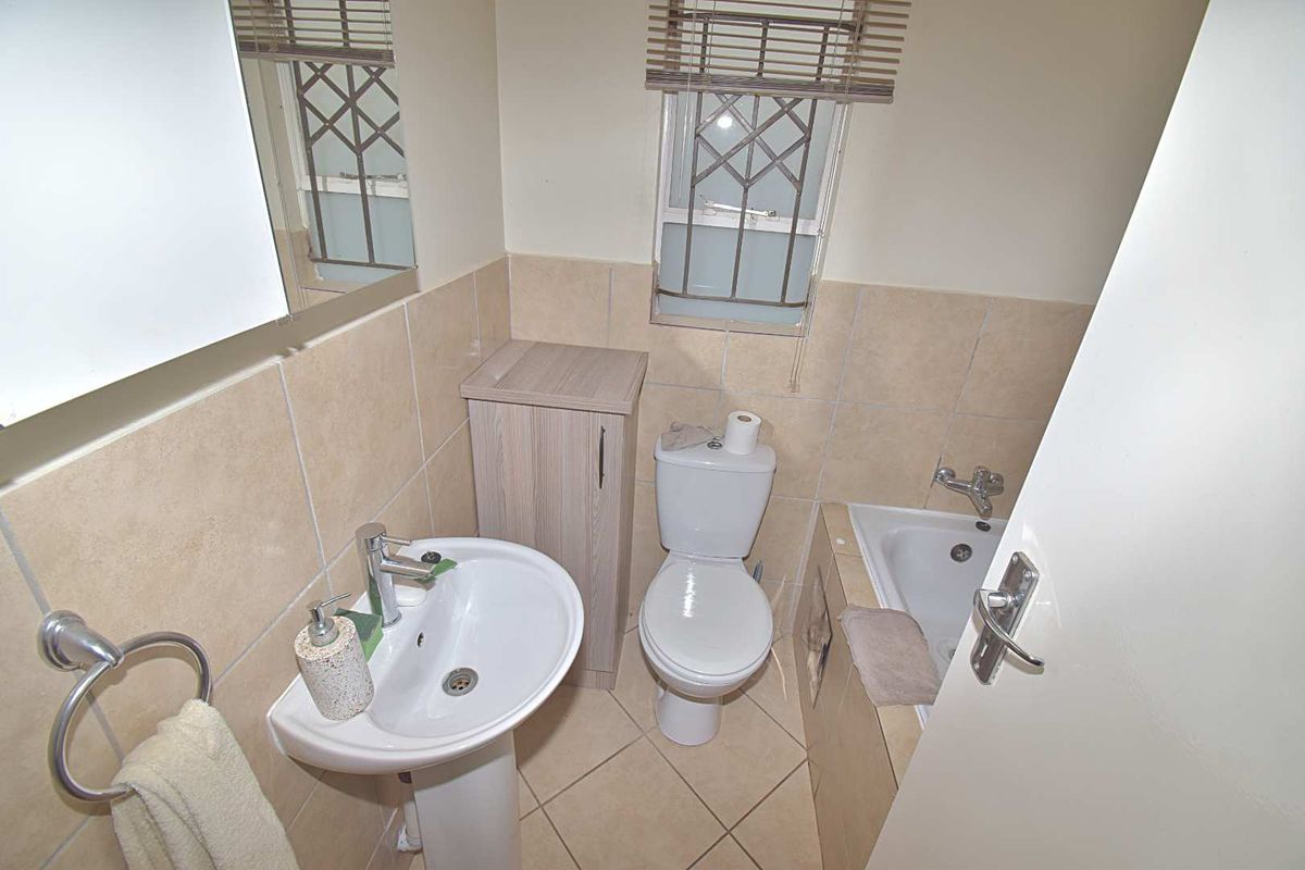 Compact bathroom featuring a pedestal basin, toilet, and a tiled bathtub with integrated shower fixtures.