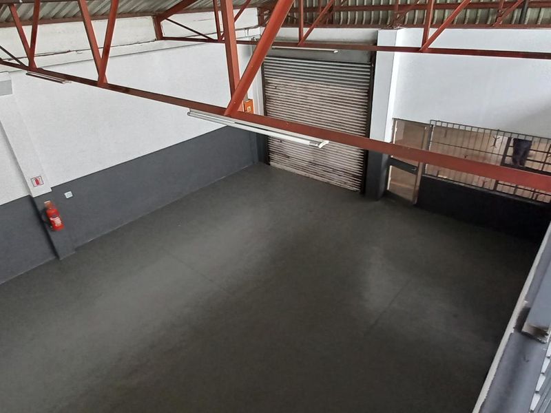 Spacious industrial utility area featuring high ceilings with exposed steel trusses, concrete flooring, and a secure roller shutter door access.