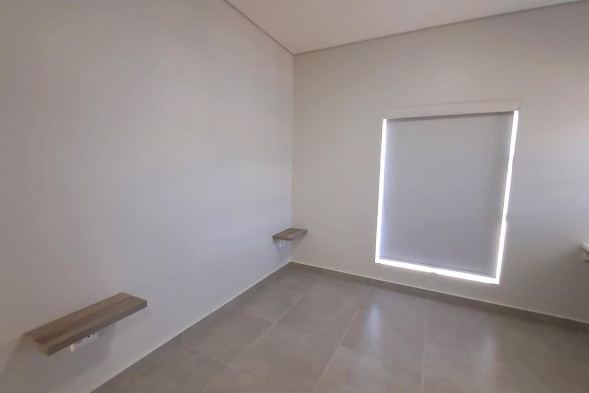 A bright, neutral-toned bedroom featuring modern tiled flooring, a fitted roller blind, and minimalist floating wall shelves.