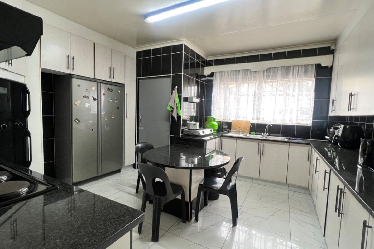 A functional kitchen featuring black granite countertops, white cabinetry, tiled flooring, and a built-in extractor fan with a dedicated breakfast nook area.