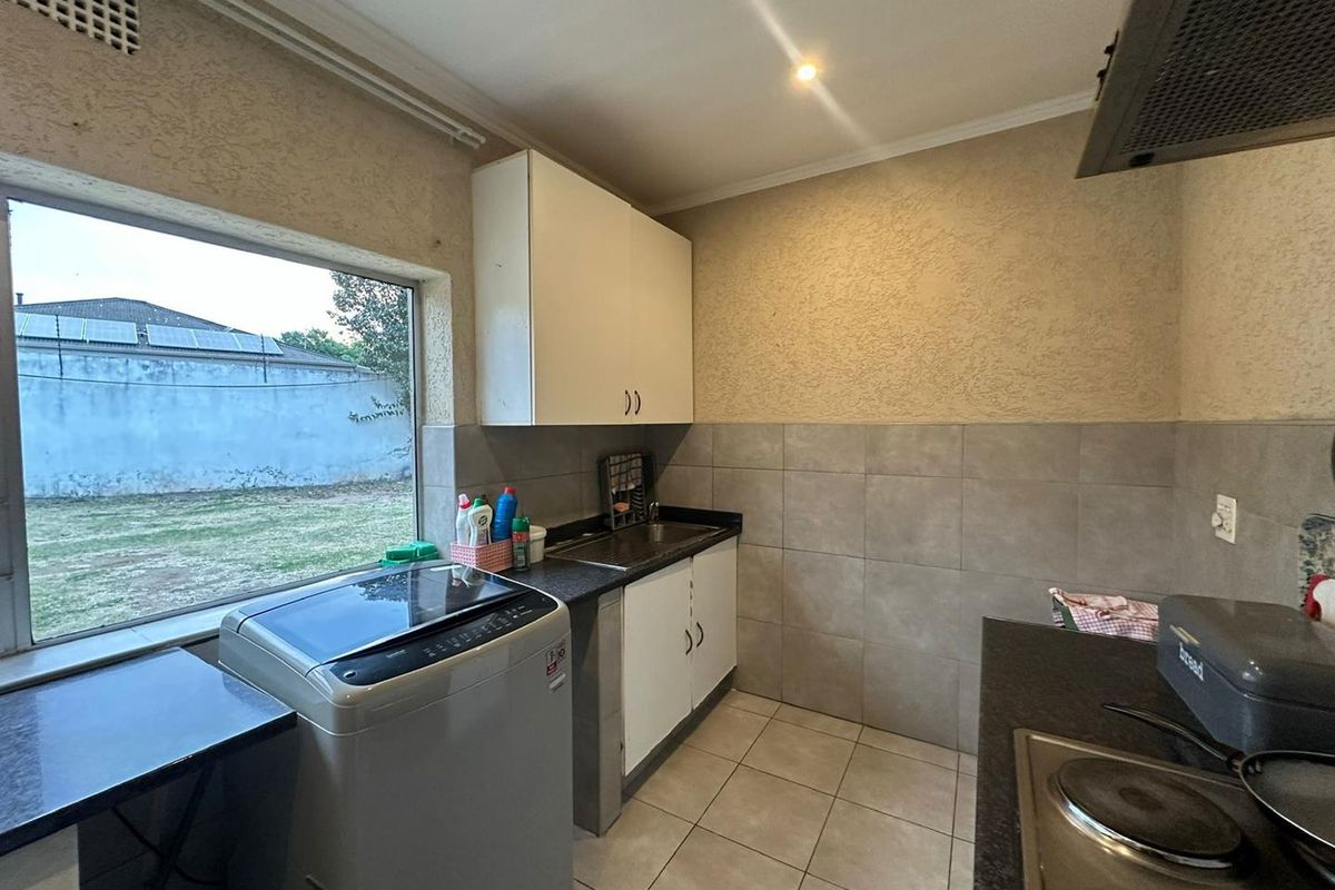 Functional kitchen and laundry area featuring tiled flooring, built-in cabinetry, a sink, and a built-in electric hob with extractor fan.