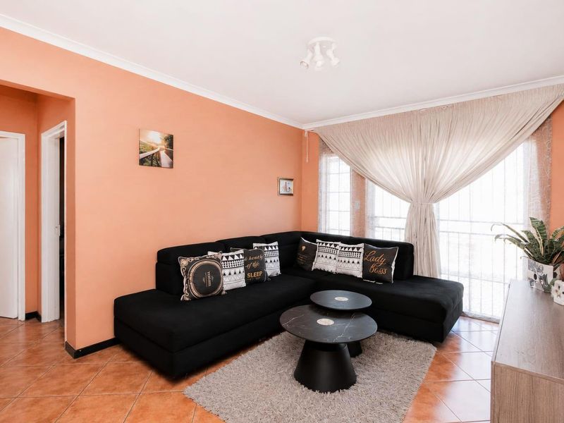 A comfortable living room featuring tiled flooring, neutral wall tones, and a large sliding glass door providing natural light.