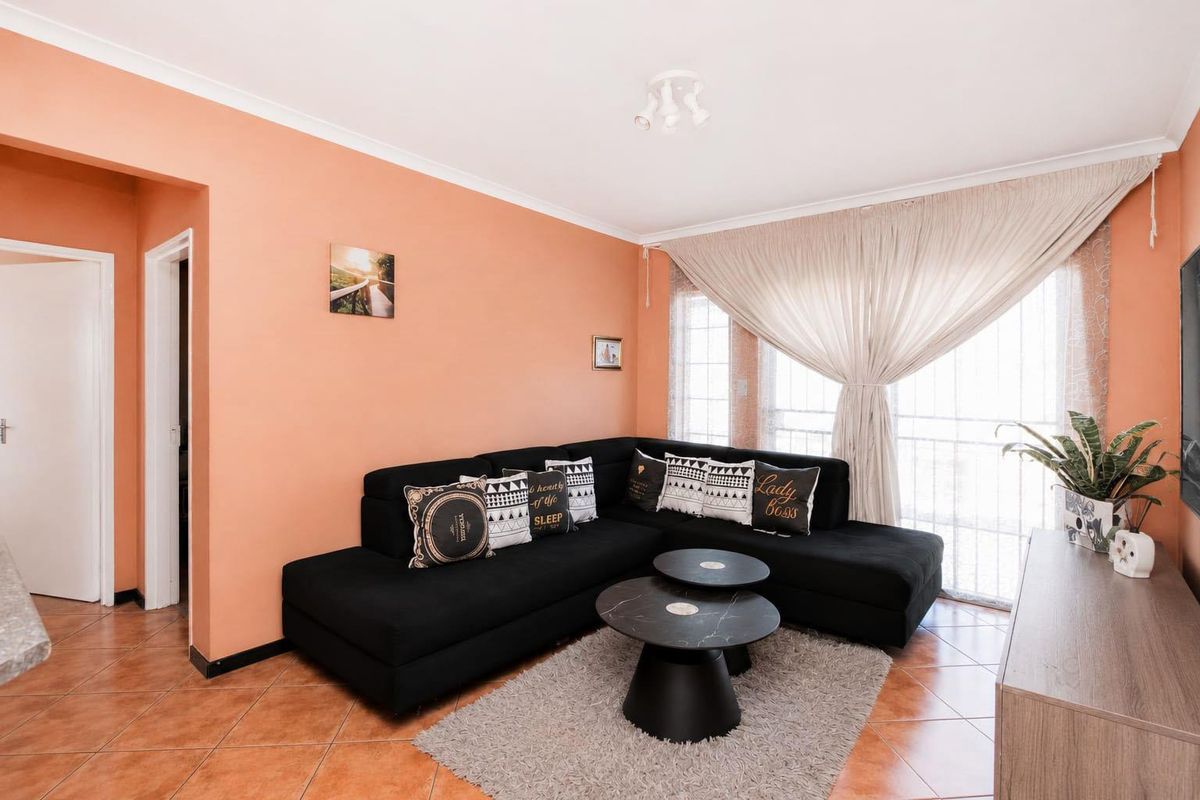 A comfortable living room featuring tiled flooring, neutral wall tones, and a large sliding glass door providing natural light.