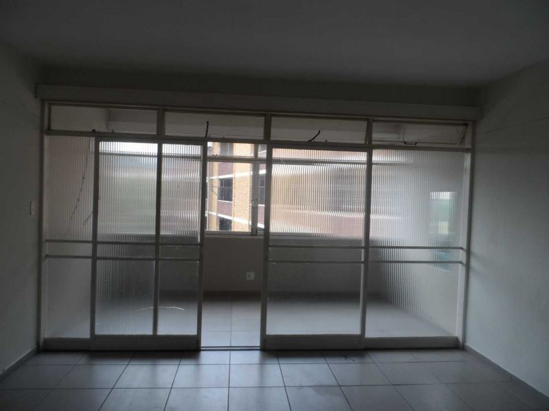 An enclosed balcony or sunroom featuring tiled flooring and sliding glass doors with transom windows, offering a view of the adjacent building.