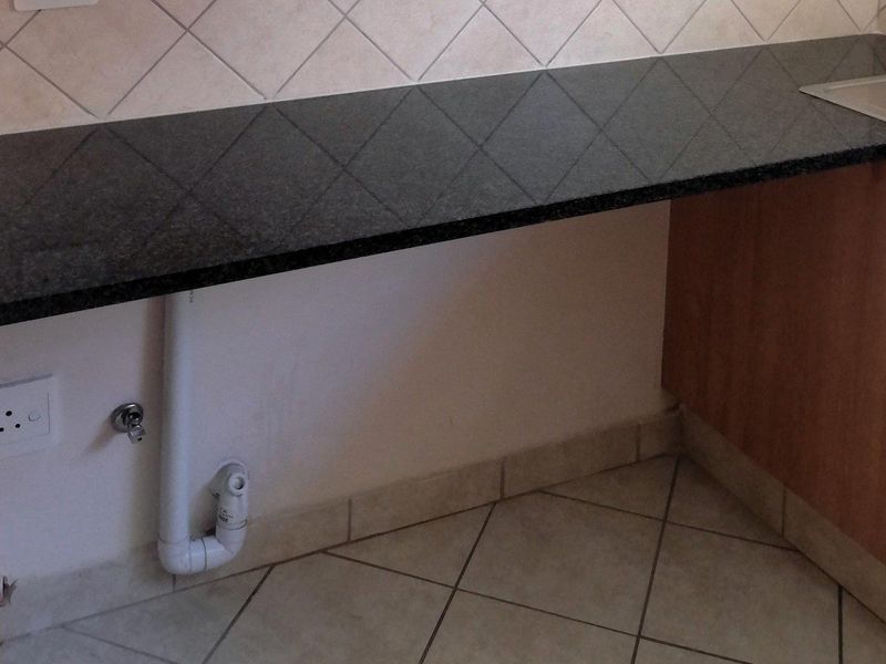 A functional kitchen area featuring dark granite countertops, a tiled backsplash, and dedicated plumbing connections for an appliance.