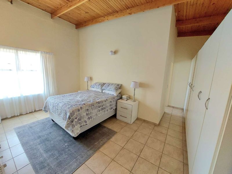 Spacious bedroom featuring high exposed timber beam ceilings, tiled flooring, and extensive built-in cupboard storage.