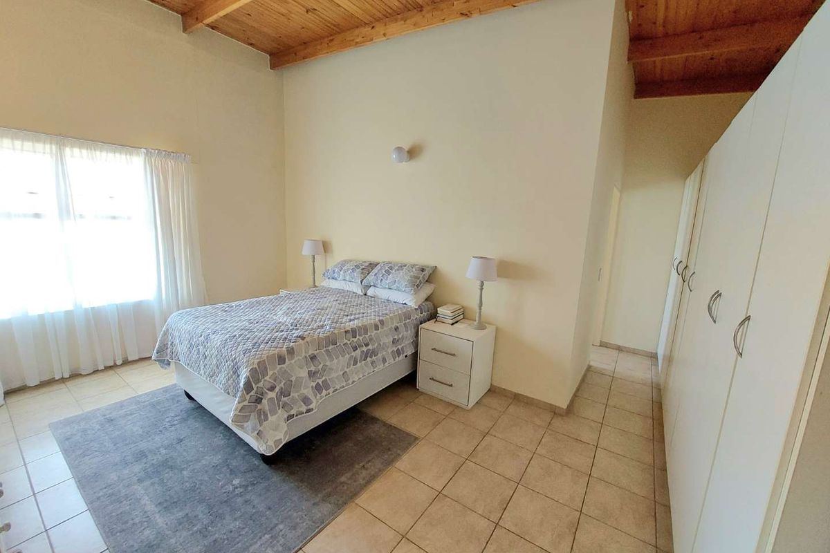Spacious bedroom featuring high exposed timber beam ceilings, tiled flooring, and extensive built-in cupboard storage.