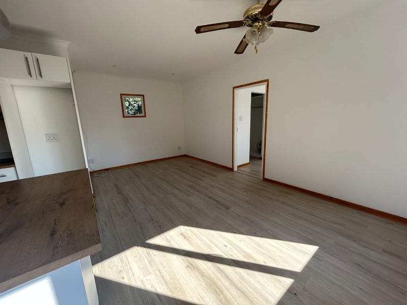 An open-plan living area featuring modern laminate flooring, a ceiling fan, and a functional kitchen corner with timber-look countertops.
