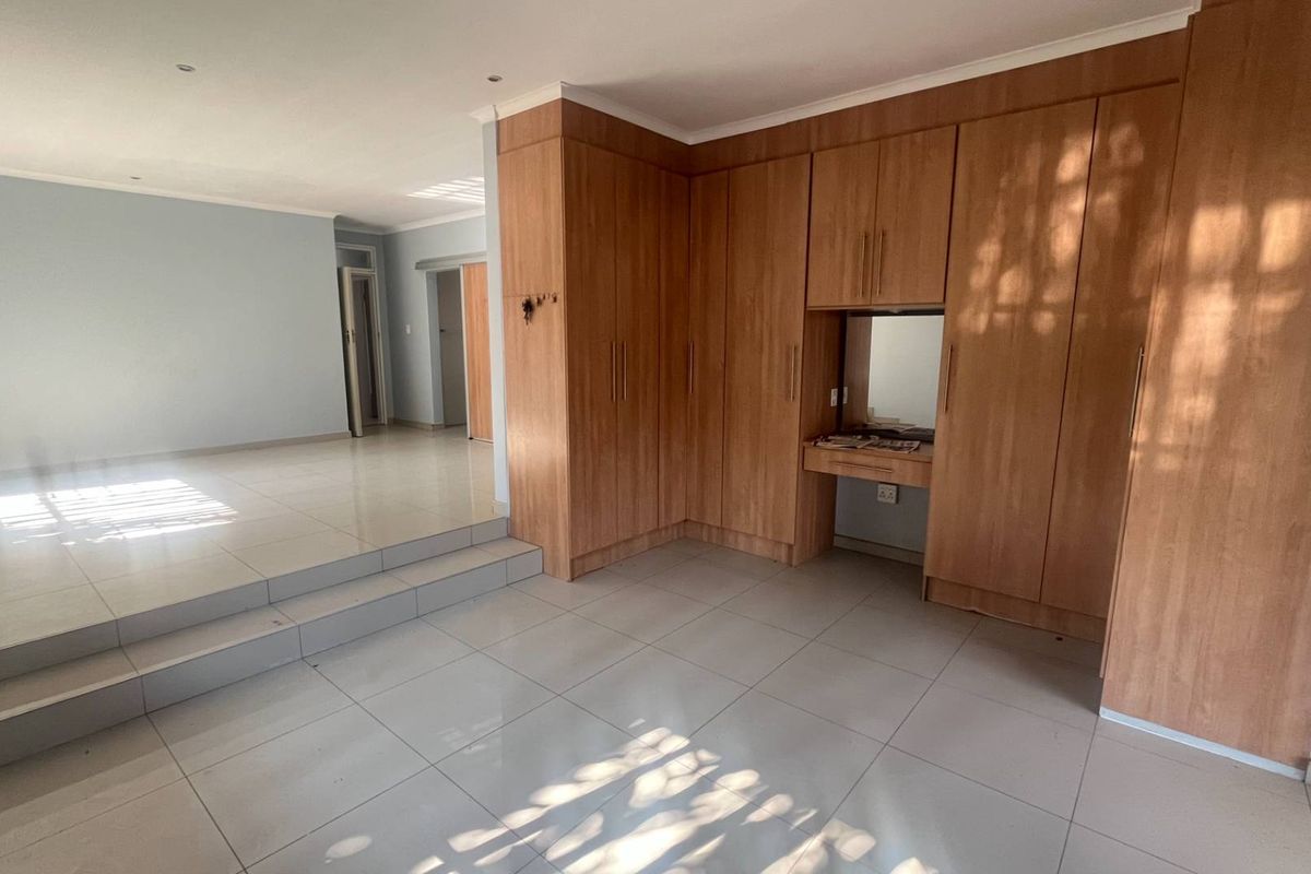 Spacious bedroom featuring built-in wooden cabinetry, a vanity area, and tiled flooring with a split-level layout.