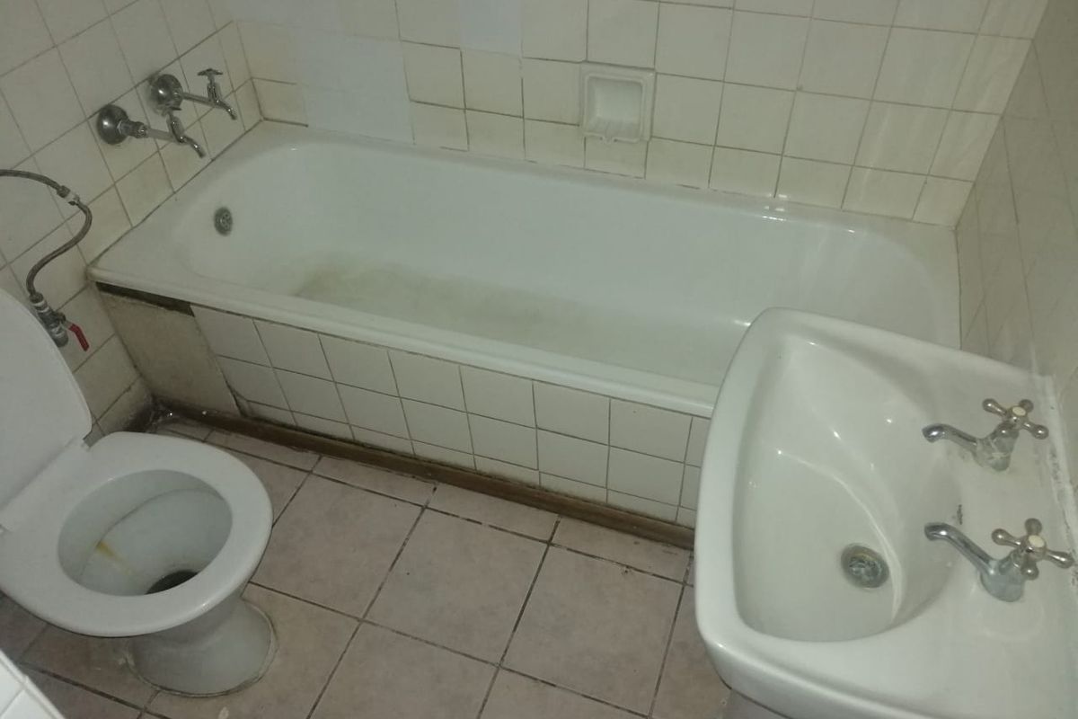 A dated bathroom featuring a standard bathtub, pedestal basin, and toilet with original wall and floor tiling.