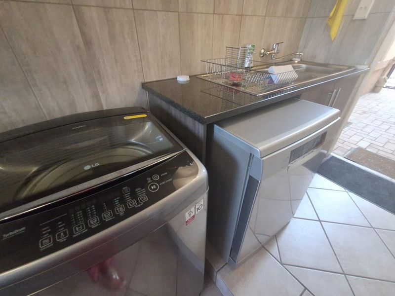 A functional laundry area featuring a granite countertop, stainless steel sink, and tiled backsplash, providing a practical space for washing and utility tasks.
