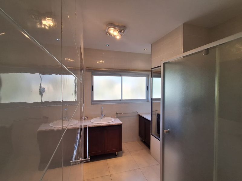 A clean, functional bathroom featuring a vanity cabinet with basin, a glass shower enclosure, and neutral wall and floor tiling.