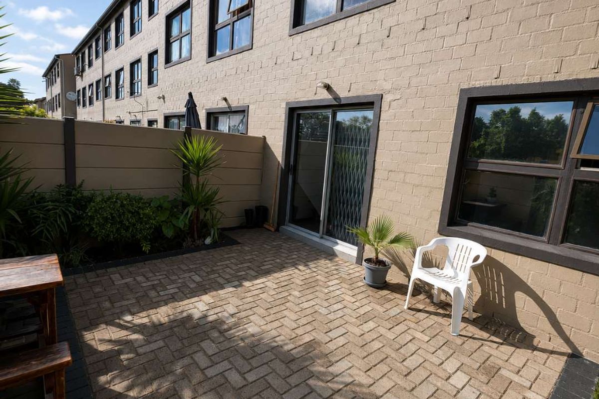 A private rear patio area featuring brick paving, a sliding glass door entrance, and a secure boundary wall.
