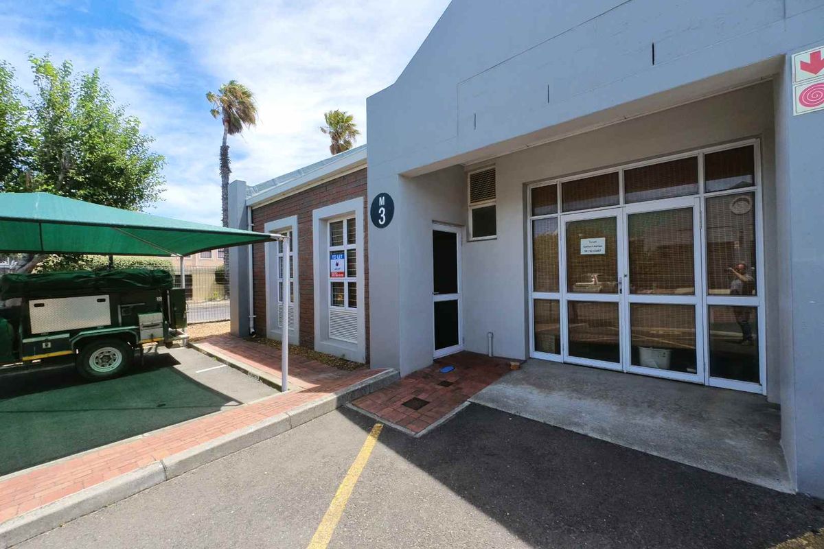 Front exterior view of an office unit featuring a glass entrance, brick accents, and a dedicated shade cloth parking bay.