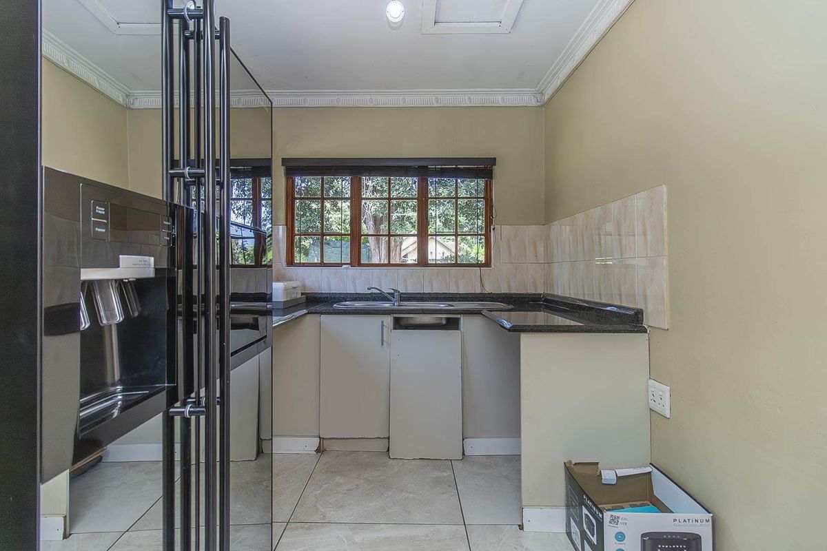 A functional kitchen featuring dark granite countertops, a stainless steel sink, and tiled splashbacks with wooden window frames.