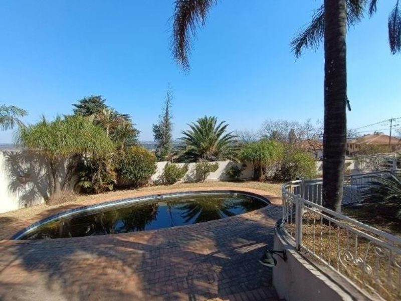 Outdoor pool area featuring a swimming pool, brick paved surround, and metal balustrade, set within a landscaped garden with perimeter walling.