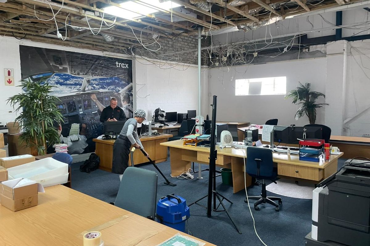 Open-plan office space featuring exposed ceiling structure, exposed electrical wiring, and carpeted flooring, currently undergoing maintenance.