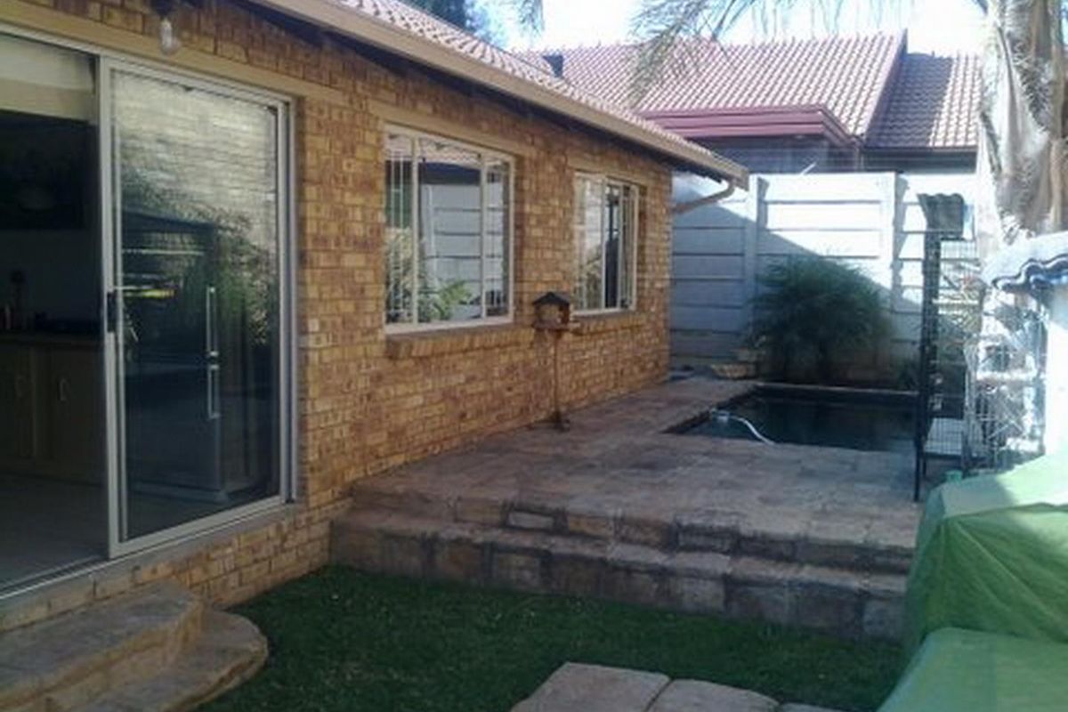 Rear exterior view of a brick townhouse featuring a paved patio area, a small plunge pool, and sliding door access to the interior.