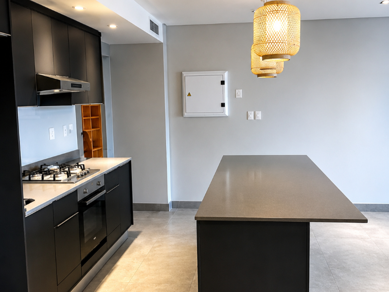 Modern kitchen featuring sleek black cabinetry, a central island with stone countertops, built-in gas hob, oven, and integrated extractor fan.