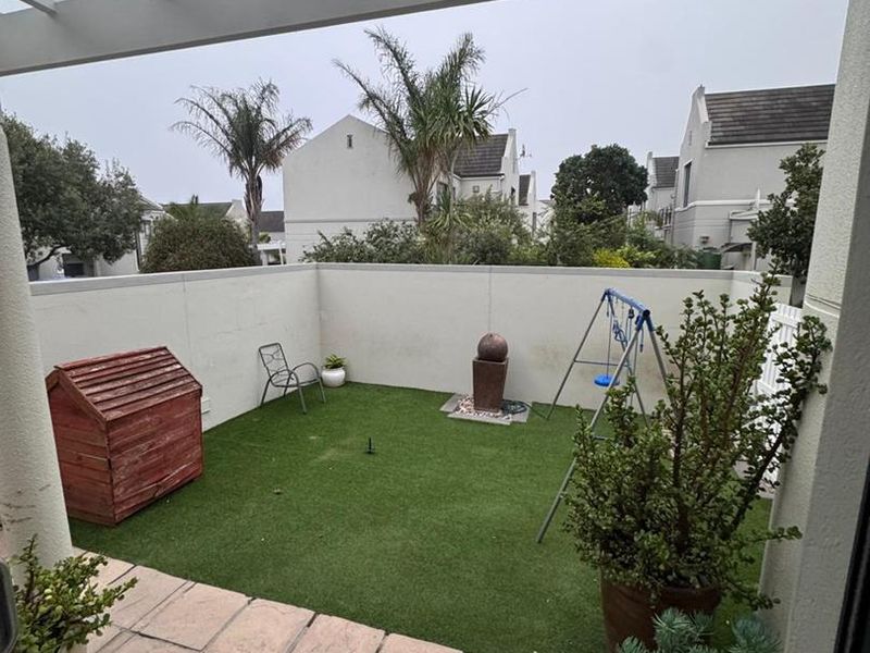 A covered patio area featuring a pergola, tiled flooring, and a private enclosed garden space with artificial turf.