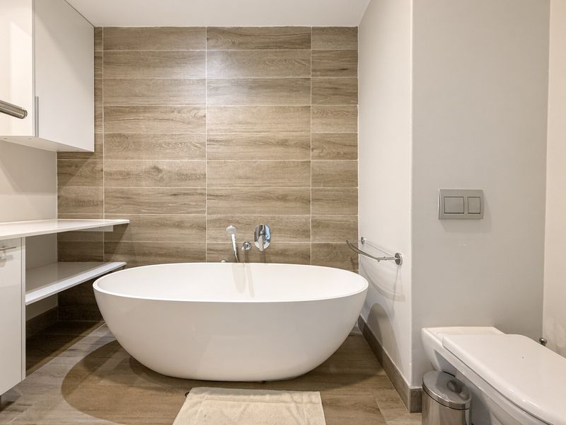 Modern bathroom featuring a sleek freestanding bathtub, wood-look tile feature wall, and integrated cabinetry with contemporary fixtures.